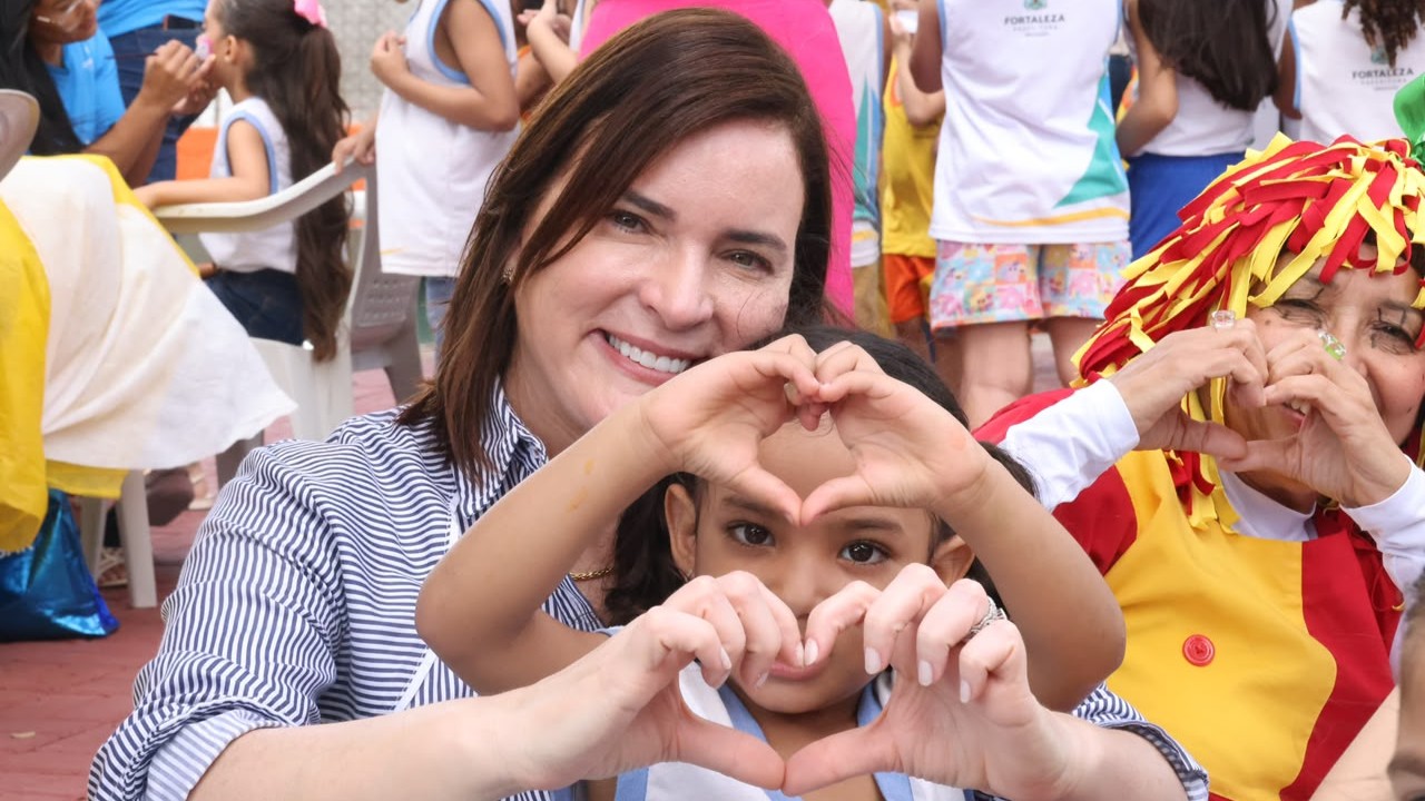 Primeira-dama Cristiane Leitão posa com uma criança; as duas estão fazendo coração com as mãos